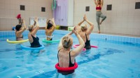Eine Masseurin und medizinische Bademeisterin trainiert eine Gruppe Senioren in einem Wasserbecken.