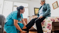 Eine Pflegefachfrau unterstützt während eines Hausbesuchs eine Seniorin beim Anziehen.