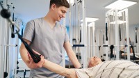 Ein Physiotherapeut einer Rehaeinrichtung unterstützt einen älteren Herrn dabei, seine Mobilität zurückzugewinnen.