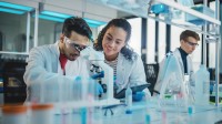 Eine biologisch-technische Assistentin unterstützt einen Naturwissenschaftler beim Mikroskopieren und Dokumentieren der Ergebnisse.
