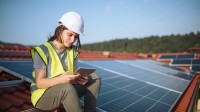 Eine technische Assistentin für regenerative Energietechnik überprüft an ihrem Tablet die richtige Einstellung der Photovoltaik-Anlage.