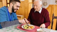 Ein Altenpfleger unterstützt einen Senior beim Mittagsessen.