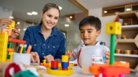 Eine Ergotherapeutin spielt mit zwei Kindern, um die Feinmotorik eines Jungen mit Bausteinen zu fördern.