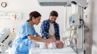 Eine Gesundheits- und Kinderkrankenpflegerin kontrolliert den Gesundheitszustand eines Neugeborenen. 