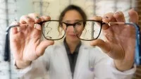 Eine Augenoptikerin reicht einem Kunden seine neue Brille zur Anprobe.