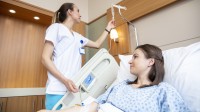 Eine Gesundheits- und Krankenpflegerin überprüft die Einstellung des Tropfes einer Patientin, die im Krankenbett liegt.