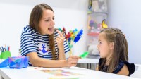 Eine Logopädin und ein Vorschulkind sitzen an einem Tisch und üben spielerisch die korrekte Aussprache von Silben.