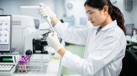 Eine medizinische Technologin in einem Laborkittel hält ein Reagenzglas mit einer Blutprobe zur Analyse im Labor.