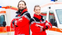 Ein Rettungssanitäterteam in rot-weißen Uniformen steht vor zwei Krankenwägen, bereit für den nächsten Einsatz.