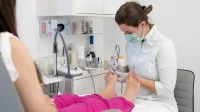 Eine Podologin behandelt die Füße einer Patientin in einer Praxis. Dabei sitzt die Patientin auf dem Behandlungsstuhl.