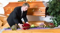 Eine Bestattungsfachkraft schmückt einen Sarg mit Blumengebinden.