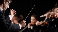 Ein Ensembleleiter hält einen Taktstock, mit dem er ein Orchester anleitet. 