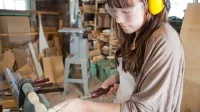 Eine Drechslerin bearbeitet ein Holzstück mit einem Drehmeißel an der Drehbank.