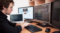 Ein Assistent für technische Informatik sitzt an seinem Schreibtisch und programmiert ein internationales Netzwerk am Computer.
