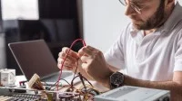 Ein Assistent für Wirtschaftsinformatik tüftelt an seinem Schreibtisch an der Hardware eines auseinandergebauten Computers.
