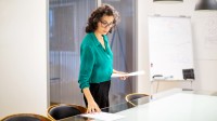 Eine kaufmännische Assistentin / Wirtschaftsassistentin platziert Dokumente auf den Tisch im Besprechungsraum.