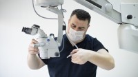 Ein technischer Assistent für medizinische Gerätetechnik wartet ein medizinisches Mikroskop. Dabei trägt er einen Mundschutz.