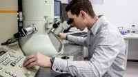 Ein physikalisch-technischer Assistent betrachtet eine Probe am Elektronenmikroskop und stellt dabei die Messwerte ein.