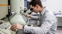 Ein physikalisch-technischer Assistent betrachtet eine Probe am Elektronenmikroskop und stellt dabei die Messwerte ein.