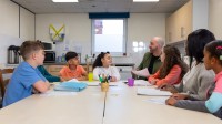 Ein Sozialassistent kümmert sich um eine Gruppe Kinder in der Nachmittagsbetreuung.