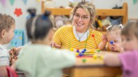 Eine sozialpädagogische Assistentin/ Kinderpflegerin spielt mit einer Kleinkindergruppe in einem Kinderhort.