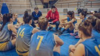 Ein Sportassistent und ein Trainiersitzen mit ihrer Mannschaft auf dem Boden der Sporthalle und besprechen.