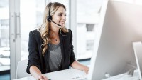 Eine kaufmännische Assistentin / Wirtschaftsassistentin für Informationsverarbeitung führt ein Telefongespräch mit einem Headset, während sie vor ihrem Computer im Büro sitzt.
