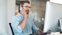 Ein kaufmännischer Assistent/ Wirtschaftsassistent für E-Business Management stimmt sich telefonisch mit einem Geschäftspartner ab.