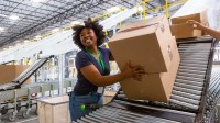 Eine Fachlageristin arbeitet in einem Logistikzentrum an einer Förderanlage für Kisten und Kartons.