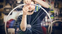 Ein Fahrradmonteur baut in seiner Werkstatt neue Speichen in die Felge eines Fahrradrads ein.