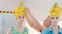 Eine Gestalterin für visuelles Marketing schmückt zwei Schaufensterpuppen mit augefallenen Kopfbedeckungen.