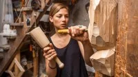Eine Holzbildhauerin bearbeitet eine Skulptur mit Knüpfel und Beitel.