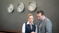 Ein Kaufmann für Hotelmanagement informiert sich bei seiner Kollegin am Empfang über die Reservierungen des Hotels, um den Personaleinsatz der nächsten Wochen besser planen zu können.