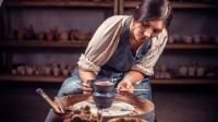 Eine Keramikerin bemalt in ihrem Atelier eine kleine Vase auf der Drehscheibe.