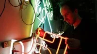 Ein Leuchtröhrenglasbläser prüft eine Neonreklame in der Neonmanufactur in Berlin.