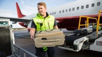 Ein Luftverkehrskaufmann hebt Gepäck von einem Flugzeug auf einen Gepäckwagen.