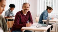 Ein Mann sitzt mit anderen in einem Klassenzimmer