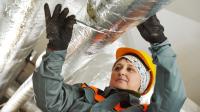 Eine Wärme-, Kälte- und Schallschutzisoliererin dämmt ein Rohr mit Glaswolle und Folie.