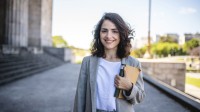 Junge Frau mit Buch steht vor einem Gebäude mit Säule