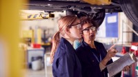 Ausbilderin und Auszubildende unter einem Auto auf hydraulischer Rampe
