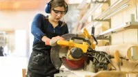 Eine junge Frau arbeitet an einer Kreissäge in einem holzverarbeitenden Betrieb.