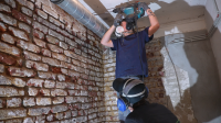 Zwei Holz- und Bautenschützer arbeiten an einer Ziegelwand.