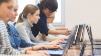 Mehrere Schülerinnen sitzen an Laptops, die Lehrerin erklärt etwas am Bildschirm einer Schülerin.