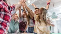 Sechs Jugendliche unterschiedlicher Herkunft und Geschlecht stehen an einem Tisch auf dem Hefte liegen und machen einen Huddle.