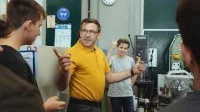 Ein Lehrer und drei Auszubildende stehen vor Maschinen und diskutieren.