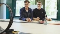 Zwei Schüler sind an einem Tisch, auf dem eine Rennbahn für Autos aufgebaut ist.