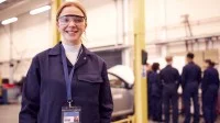 Junge Frau mit anderen Auszubildenden in einer Autowerkstatt