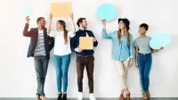 Fünf junge, fröhliche Menschen lehnen an einer Wand halten Sprechblasen aus Papier hoch.