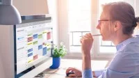 Eine Frau organisiert Termine, Aufgaben und Arbeitszeiten am Computer mit einem digitalen Kalender.