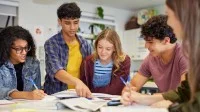 Fünf Schülerinnen und Schüler arbeiten zusammen an einem Tisch mit Heften und Büchern.